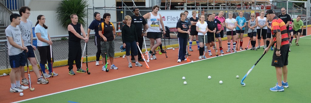Jack Clayton showing a group of enthusiastic players how to use a hockey stick.